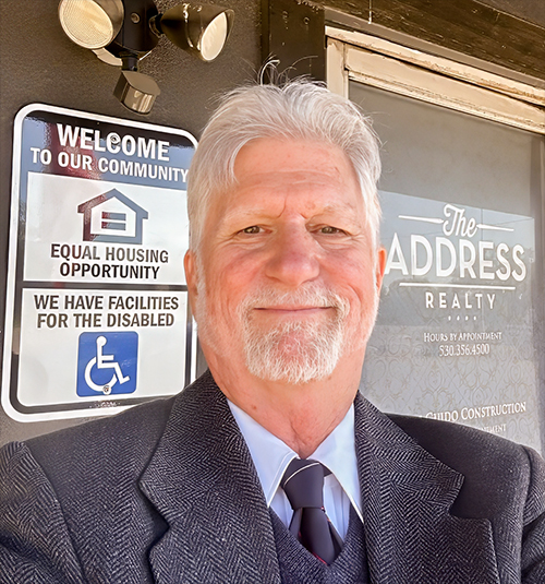 Skip Murphy of The Address Realty poses in front of his office with accessibility signage clearly visible.